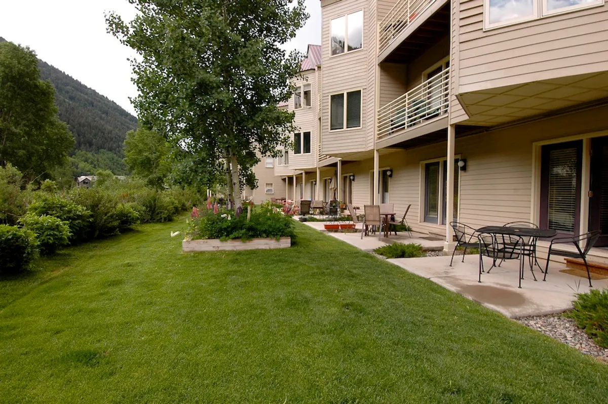 A sunny lawn with patio furniture set up for relaxation, surrounded by greenery and offering a clear mountain view. The inviting patio area emphasizes easy access to the outdoors and spaces ideal for family gatherings or quiet moments.