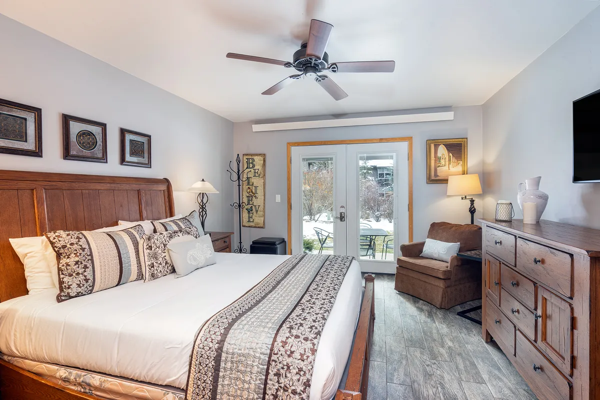 A cozy condo bedroom featuring a comfortable bed, a stylish dresser, and sliding glass doors that open to a private patio. Soft morning light fills the room, inviting guests to enjoy a peaceful start to their day with a view of the outdoors.