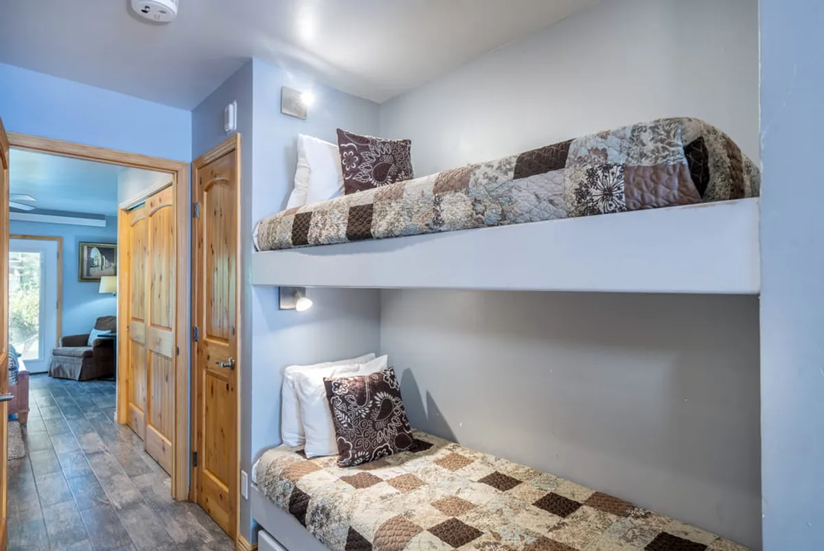 A cozy hallway nook featuring twin bunk beds with decorative pillows and a wooden door nearby. The space is styled for comfort and is clearly designed with children or small guests in mind, making it ideal for family stays.
