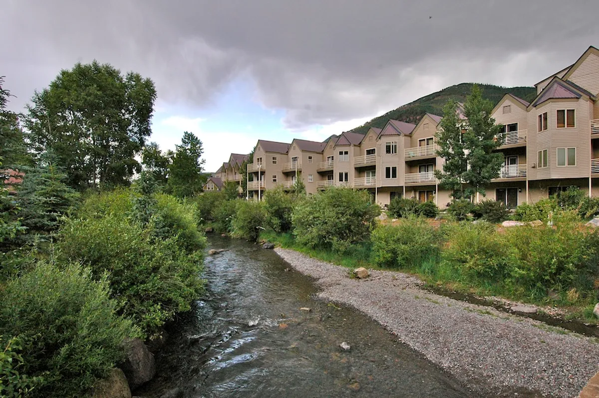 A peaceful exterior view showing the stream running alongside Viking Lodge, with buildings nestled among lush trees and balconies overlooking the water. The surrounding greenery and tranquil stream create an inviting atmosphere for outdoor exploration.