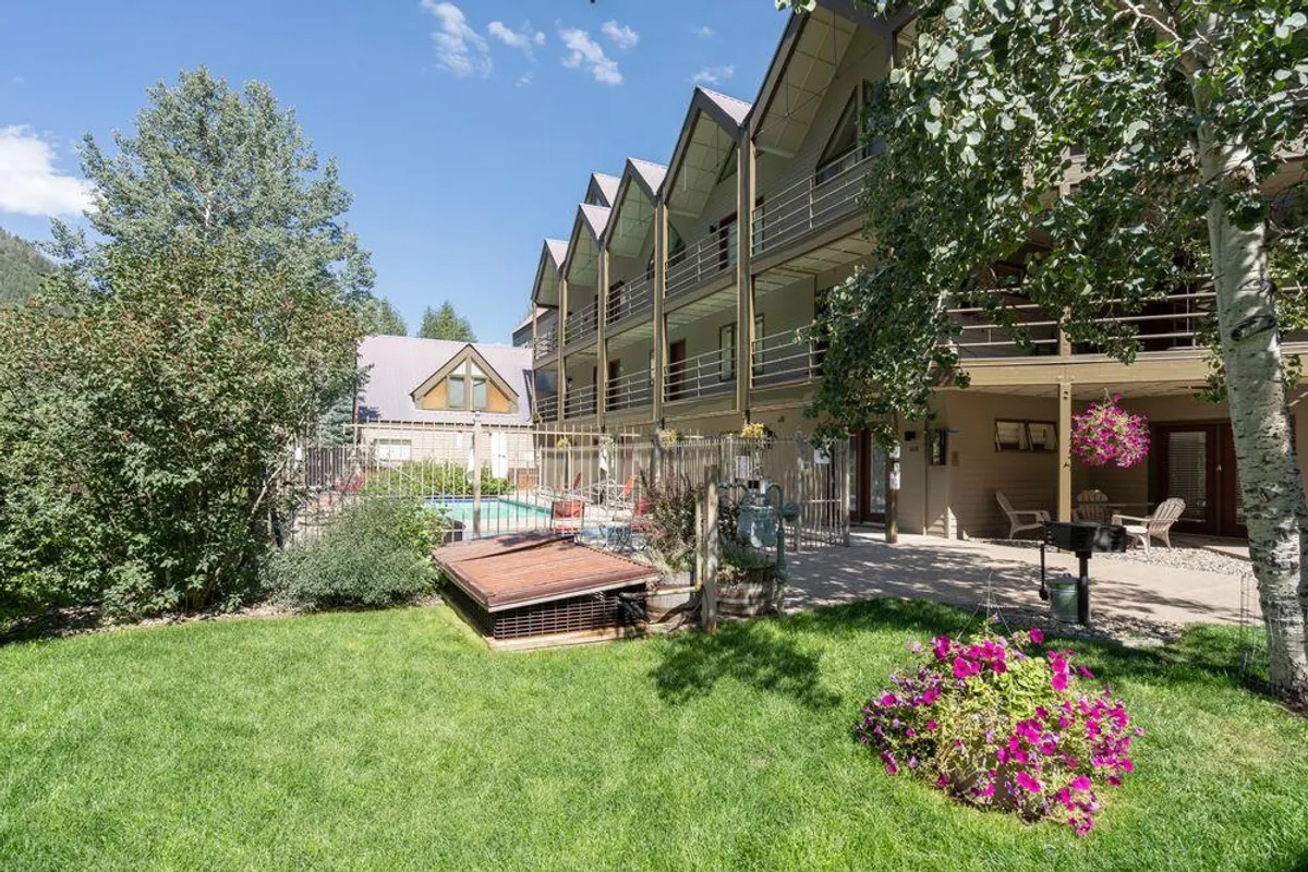 A refreshing outdoor pool area bordered by vibrant flower beds, with balconies overlooking the scene. The pool is surrounded by lounge chairs, suggesting a communal spot for relaxation and socializing. The sunny atmosphere captures the essence of summer leisure.